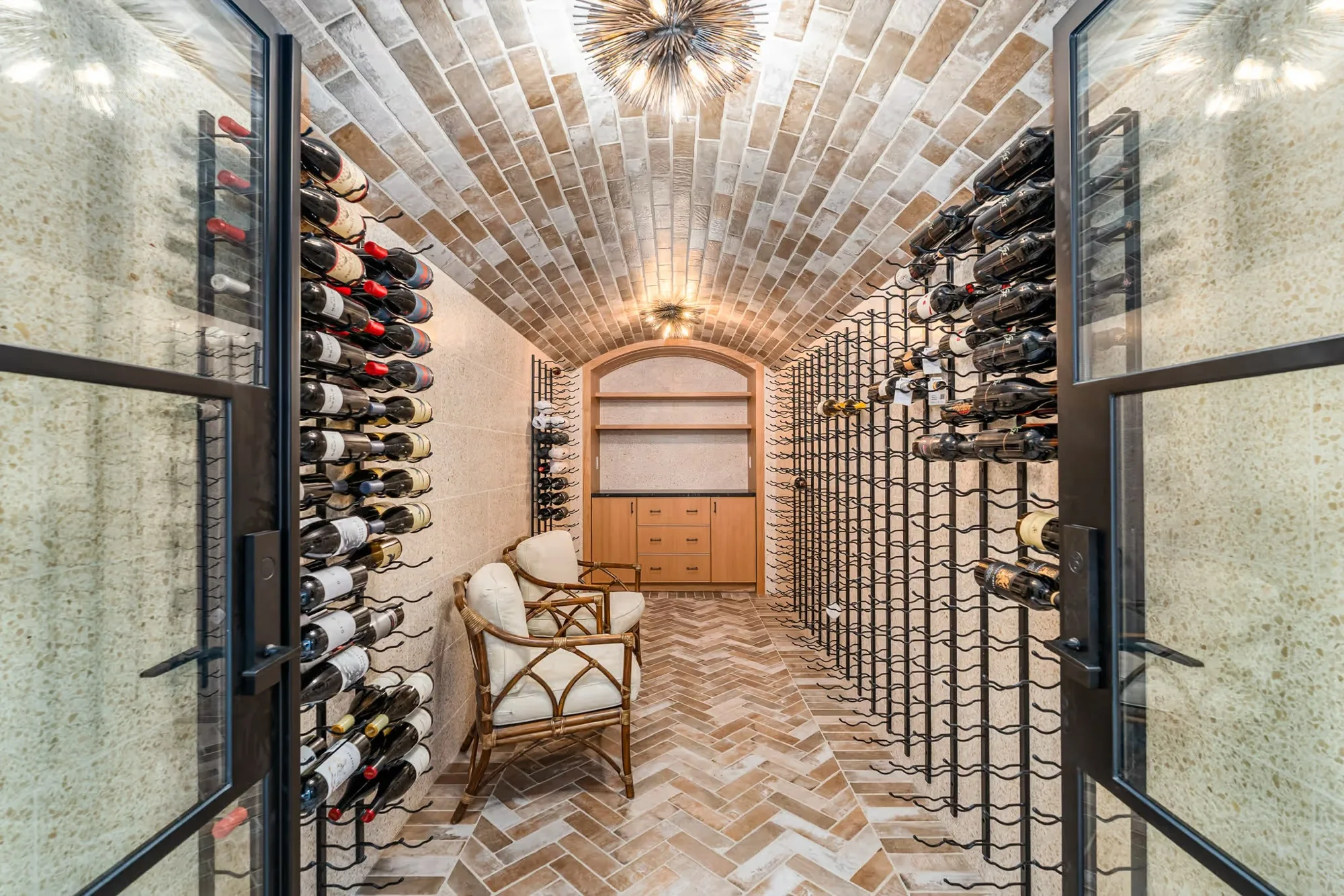 Barrel-vaulted brick wine cellar with iron racking, a glass door and a herringbone floor