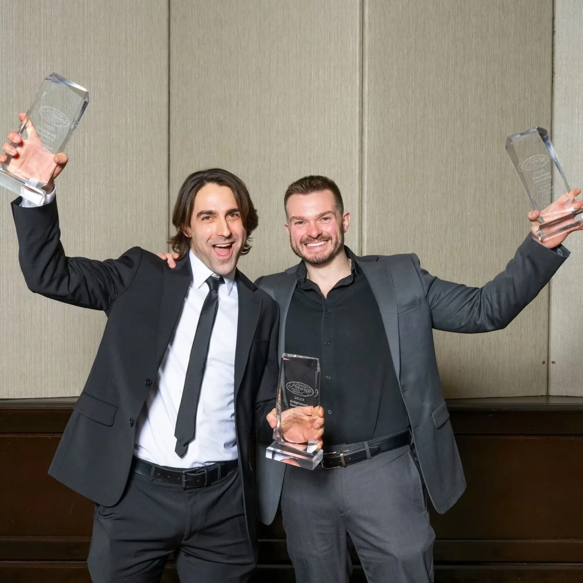 Two people in suits holding up glass awards at an awards ceremony