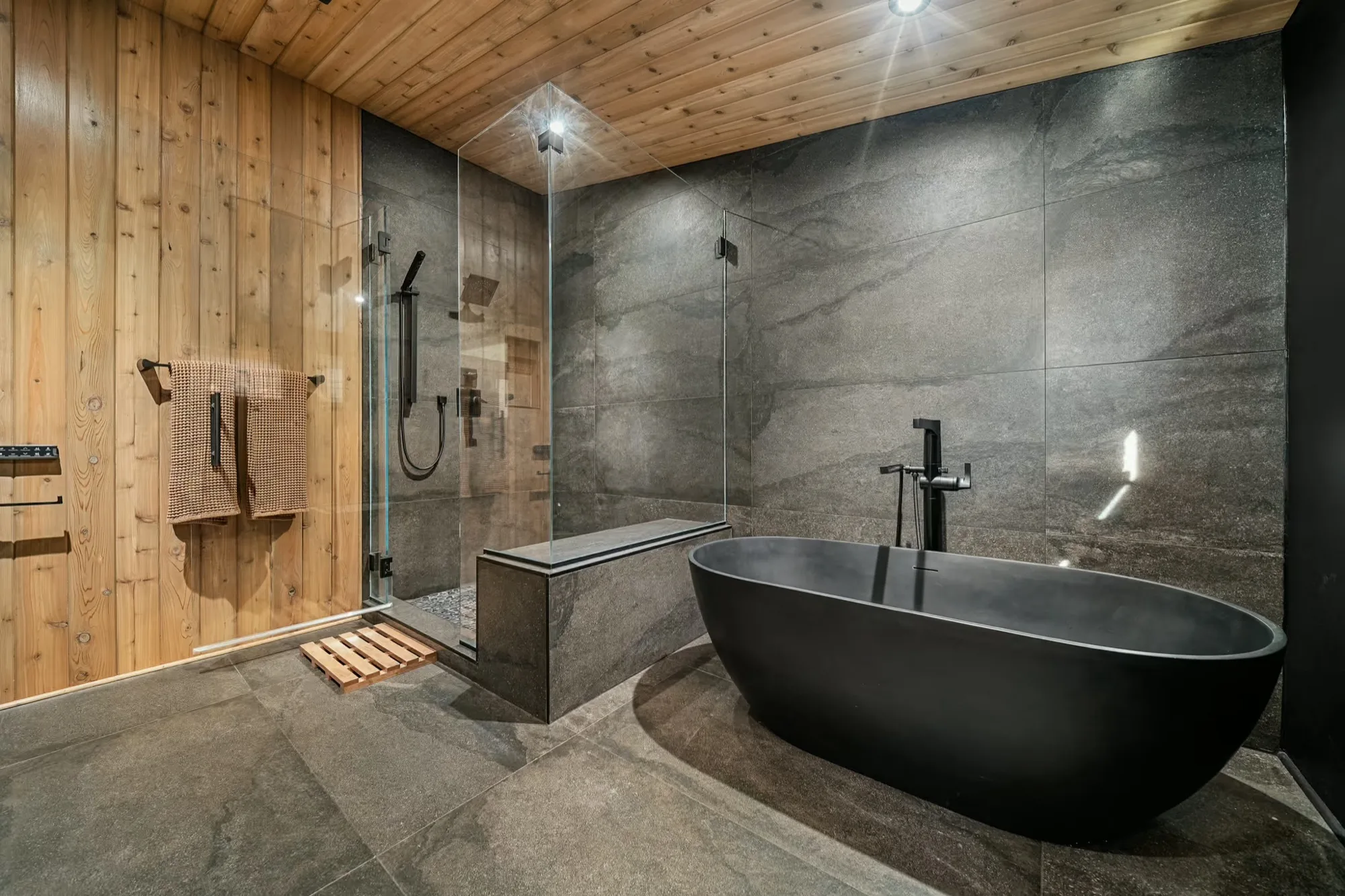 Master bathroom with large-format black tile, a freestanding tub and warm wood paneling running across the wall and slanted ceiling