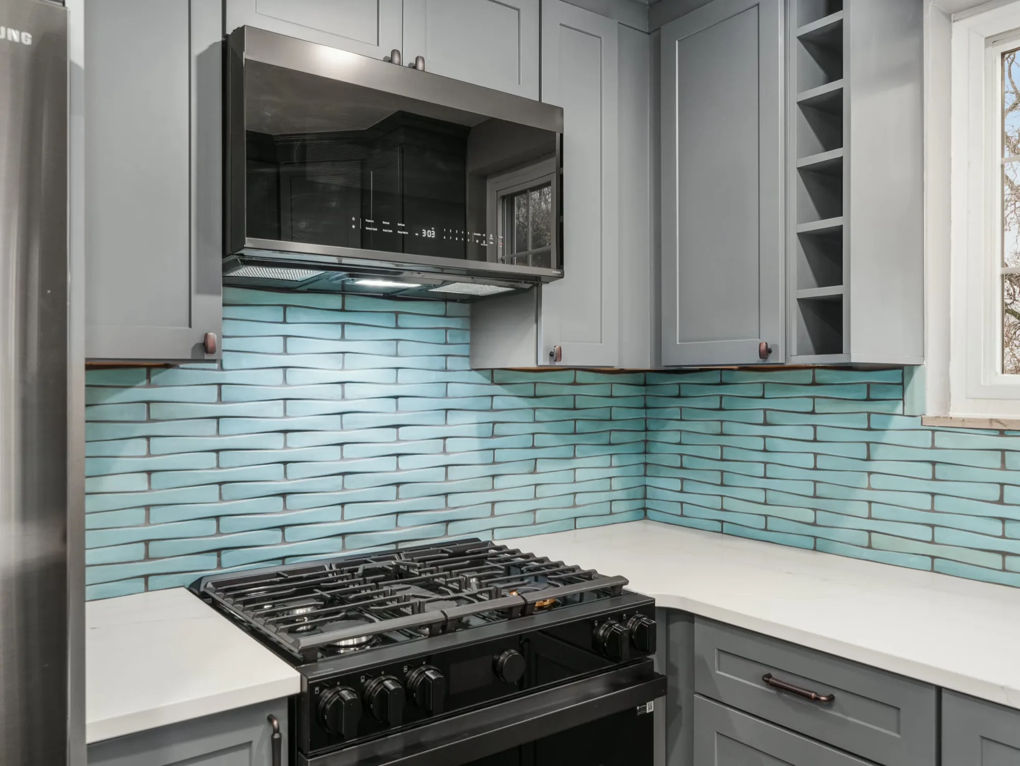 Grey shaker kitchen with a dimensional aqua backsplash, white quartz counters and black appliances