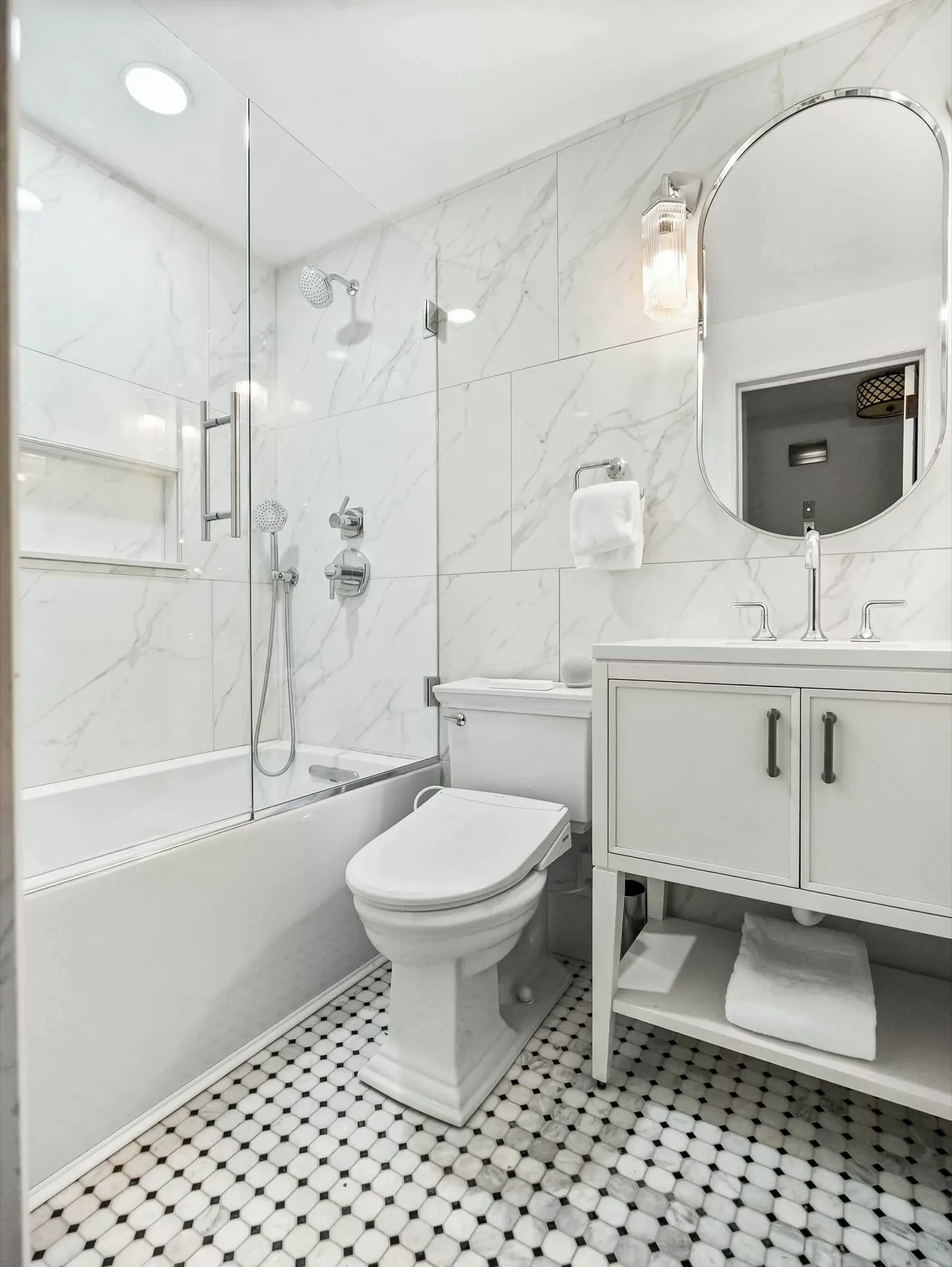 Bathroom with white marble-look shower tile, a black and white hexagon mosaic floor and polished chrome fixtures