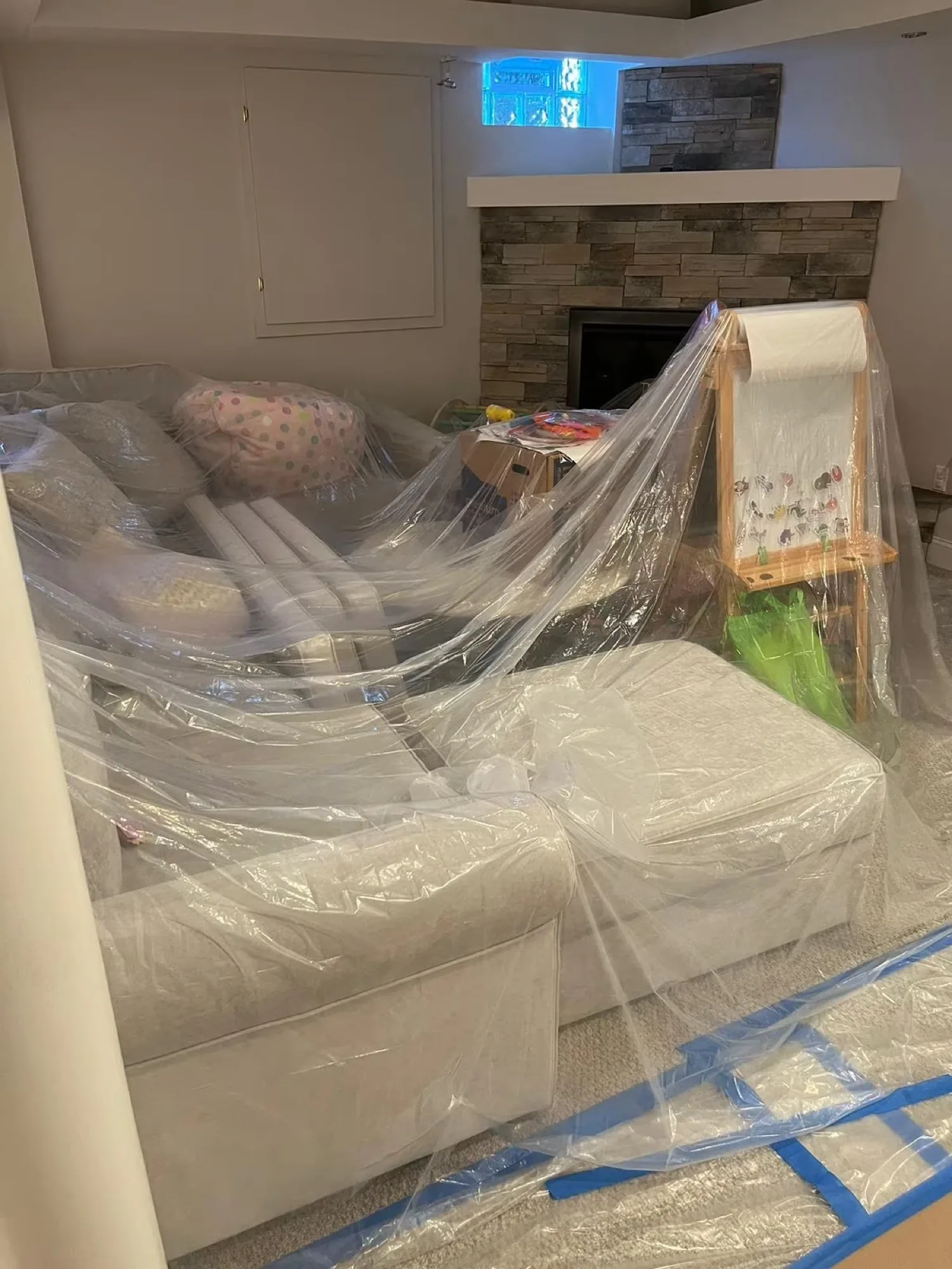 Sofa and lower-level furniture sealed under plastic sheeting with taped floor protection
